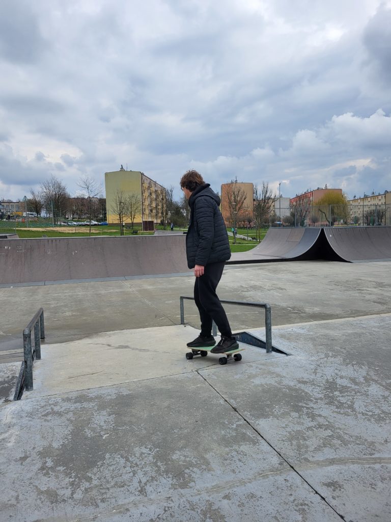Skatepark: Busko Zdrój - widok ze schodów. Młody chłopak jadący na desce surfskate.